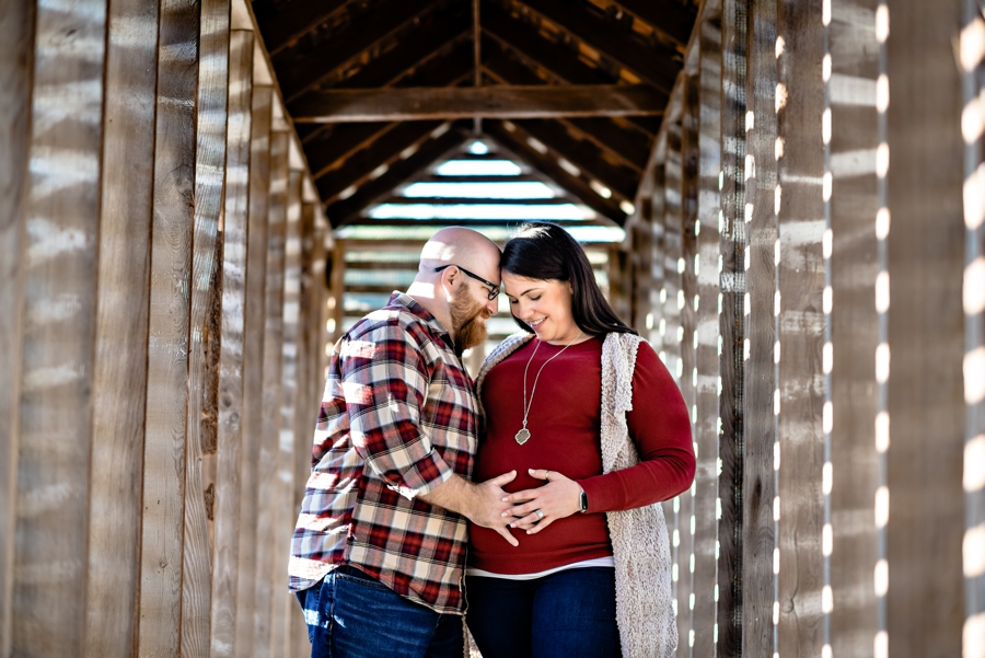 A young pregnant couple holding each other in a chicken coop at valley forge state park.